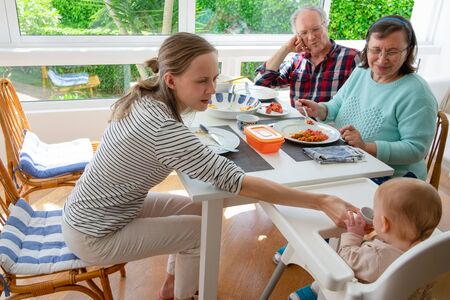 Family gathering for lunch at home. Mom teaching baby daughter drink from cup. Grandma and grandpa...