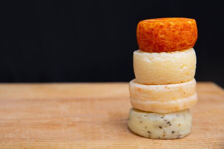 Stack of whole spicy cheeses on wooden table against dark wall background. Closeup, side view, copy space. Cheese dairy advertising conceptの写真素材