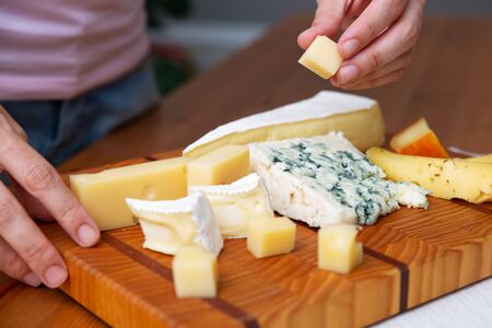 Woman taking piece of cheese from wooden board. Blue, soft and hard cheeses. Studio shot. Selective focus. Side view. Dairy meal and cooking on isolation concept for flyers and bannersの写真素材