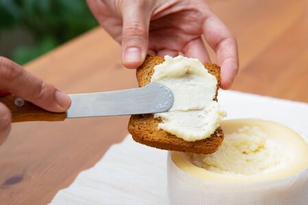 Female hands spreading soft cheese on toasted bread. Traditional rustic breakfast. Studio shot....