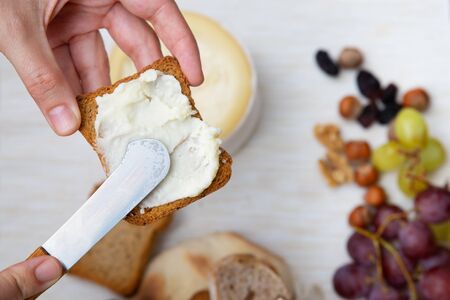 Woman spreading soft cheese on toasted bread. Traditional rustic breakfast. Studio shot. Selective focus. Top view. Dairy meal and cooking on isolation concept for flyers and bannersの写真素材