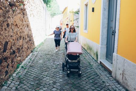 Young mother walking with stroller and her parents in street. Woman walking with baby outside. Family leisure conceptの写真素材