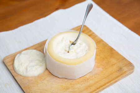 Soft cheese with cut top standing on wooden board. Traditional rustic breakfast. Studio shot....