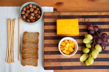 Yellow cheese and grapes laying on wooden board. Nuts and toasted bread laying on white cloth. Studio shot. Top view. Dairy meal and cooking on isolation concept for flyers and bannersの写真素材