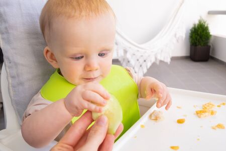 Hand of mom giving slice of fresh vegetable to baby, feeding daughter during lunch time. First solid food or child care at home conceptの写真素材