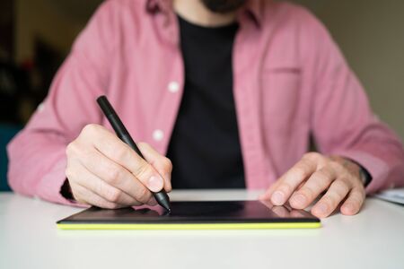 Unrecognizable focused guy drawing on graphic tablet. Male hands holding stylus and electronic tablet. Working at home and technology conceptの写真素材