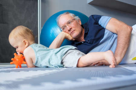 Lovely red-haired newborn lying on belly and playing with toy. Baby on soft floor. Serious...