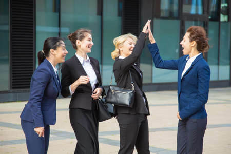 Happy excited business ladies giving high five. Businesswomen wearing suits meeting in city, celebrating success. Team success and teamwork conceptの写真素材