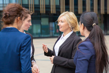 Female business partners discussing deal outdoors. Businesswomen wearing suits standing together in city and talking. Corporate communication conceptの写真素材