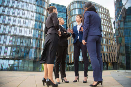 Confident business ladies group discussing contract outdoors. Businesswomen wearing suits standing together in city and talking. Low angle. Cooperation and teamwork conceptの写真素材