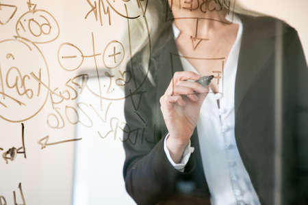 Unrecognizable grey-haired businesswoman writing on glass board. Hand holding black marker and making notes for project. Strategy, business and management conceptの写真素材