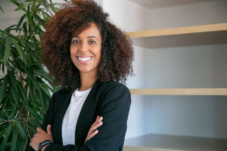 African American curly businesswoman standing with folded hands. Portrait of successful confident...