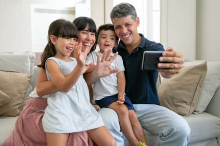 Cheerful parents couple and two children sitting on couch at homeの写真素材