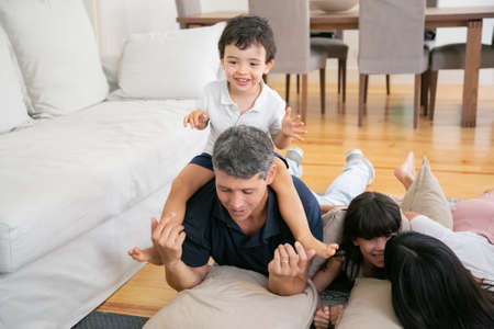Happy family with two little kids having fun at home, lying on floor together. Little son sitting on...