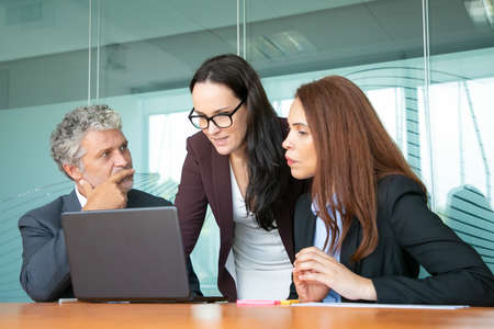 Project manager showing presentation on laptop to colleagues. Business team sitting and standing at...