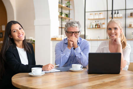 Business colleagues or partners of different ages meeting over cup of coffee at co-working, sitting...