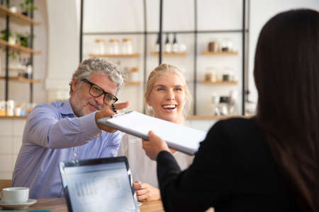 Insurance agent meeting with young and mature customers at co-working, giving agreement for signing. Businesswoman using laptop with graphs on display. Business meeting conceptの写真素材