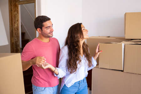 Happy handsome young man showing new apartment with carton boxes to his excited cheerful girlfriend....