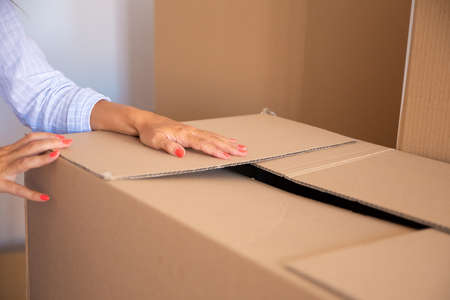 Woman packing things for moving. Closeup of female arms on carton box. Cropped shot. Relocation or...