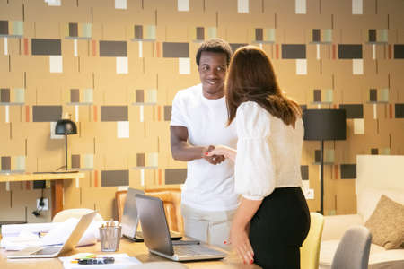 African American designer smiling and greeting female client. Happy young people standing indoors, handshaking and meeting in coworking space. Communication, design and teamwork conceptの写真素材