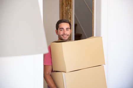 Happy man moving into new apartment, walking through doorway and carrying boxes. Side view. Loader occupation or delivery service conceptの写真素材