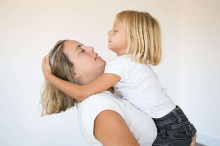 Beautiful blonde mother holding daughter and looking at her. Portrait of Caucasian mom hugging or...