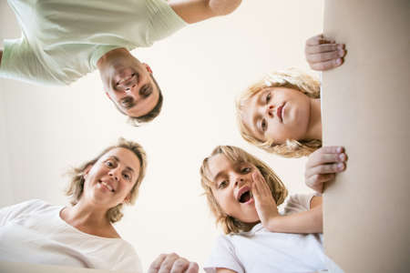 Exited family with cute children looking inside carton box. Happy Caucasian blond mother, father and two daughters opening box and smiling. Bottom view. Unpacking, relocation and moving day conceptの写真素材