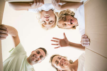 Happy family with cute children opening moving cardboard box and looking inside. Caucasian parents and lovely daughters unpacking box and smiling. View from inside. Relocation and moving day conceptの写真素材