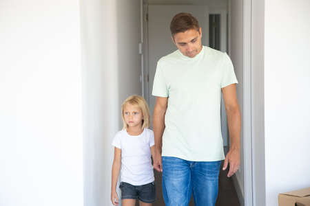 Dad leading pretty fair haired daughter into their new apartment, holding hand, walking in corridor....