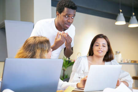 Designers team meeting and arguing about project. Diverse colleagues standing and sitting at table with laptops, looking and pointing at screen, talking and gesturing. Corporate meeting conceptの写真素材