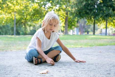 Serious sweet fair haired girl sitting and drawing with colorful pieces of chalks. Copy space. Childhood and creativity conceptの写真素材