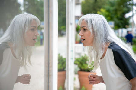 Excited female shopaholic staring at shop window with open mouth, standing at store outside. Side...