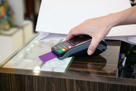 Shop cashier offering customer to enter pin code while operating payment process. Cropped shot,...