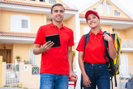 Cheerful post workers standing, smiling and working together. Happy couriers delivering order in...