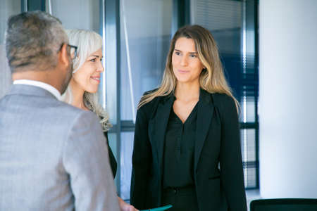 Businesswoman standing in office and talking with colleagues. Young confident employee meeting with professional grey-haired businesspeople and discussing work. Business and communication conceptの写真素材