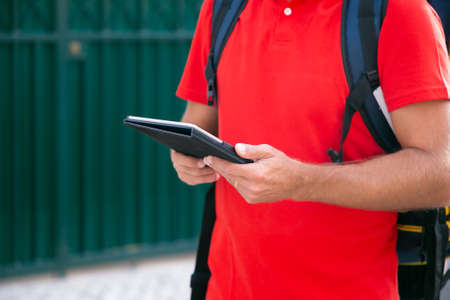 Unrecognizable courier standing and holding tablet in hands. Cropped view of deliveryman delivering...