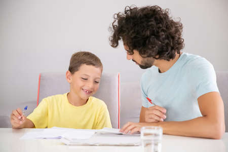 Happy boy and his dad doing school home task together, writing in papers and discussing lesson. Family and gay parents conceptの写真素材