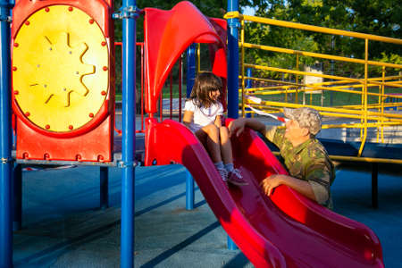 Happy military father enjoying time with daughter in playground, while girl sliding. Copy space....