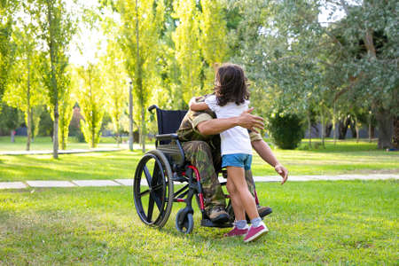 Disabled retired military man meeting and hugging little daughter in park. Veteran of war or returning home conceptの写真素材