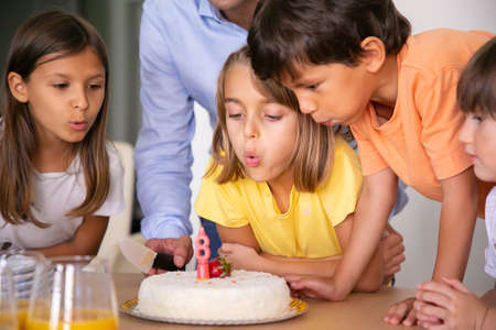 Lovely kids blowing out candle and making wish. Blonde Caucasian girl celebrating her birthday with...