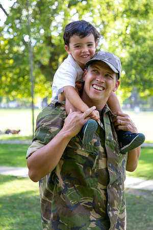 Caucasian dad holding son on neck and smiling. Happy cute boy hugging father in military uniform....