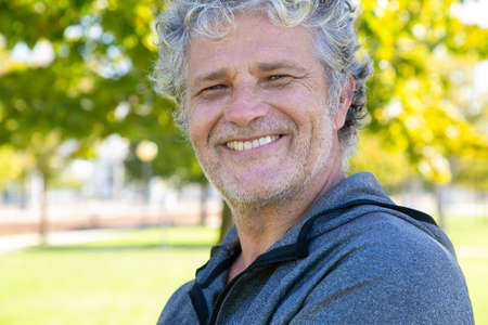 Happy grey haired man in sportswear standing outside, looking at camera and smiling. Closeup shot....