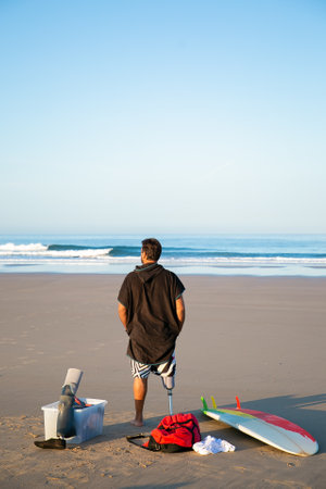 Back view of male surfer wearing artificial limb, standing on sand by surfboard. Vertical shot. Artificial limb and active lifestyle conceptの写真素材