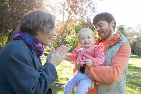 Happy mom and dad playing with cute baby girl in autumn park, holding kid who looking at camera and smiling. Medium shot. Family and childhood conceptの写真素材