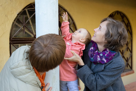Joyful young couple and toddler girl walking near museum building in park, touching columns. Medium shot. Family portrait conceptの写真素材