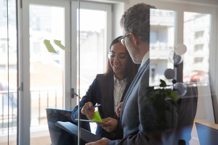 Cheerful office employees sticking stickers on glass wall. Confident young businesswoman in...