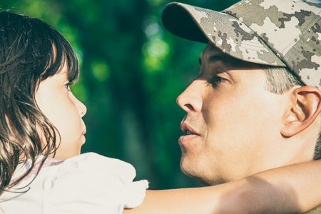 Joyful military dad holding little daughter in arms, hugging girl outdoors after returning from mission trip. Closeup shot. Family reunion or returning home conceptの写真素材