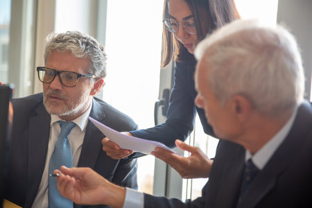 Serious female assistant giving paper reports to mature business men for studying. Closeup shot. Business and paperwork conceptの写真素材