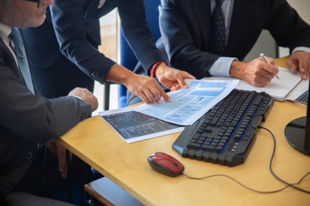 Investors and consultant discussing trading strategy, pointing at papers with financial charts and pens. Cropped shot. Broker job or investment conceptの写真素材