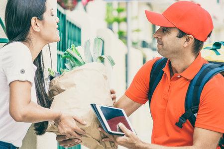 Happy female customer receiving food from grocery store, taking package from courier at her gate. Shipping or delivery service conceptの写真素材